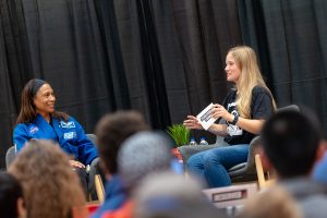 Two seated women engage in conversation on a stage.