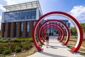 12 feet tall red rings in front of a university building with a sign that says Do Good.
