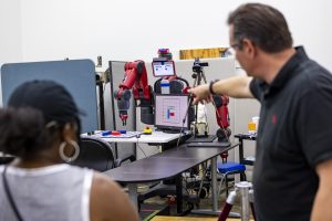 A professor encourages a student to play a game with a robot.