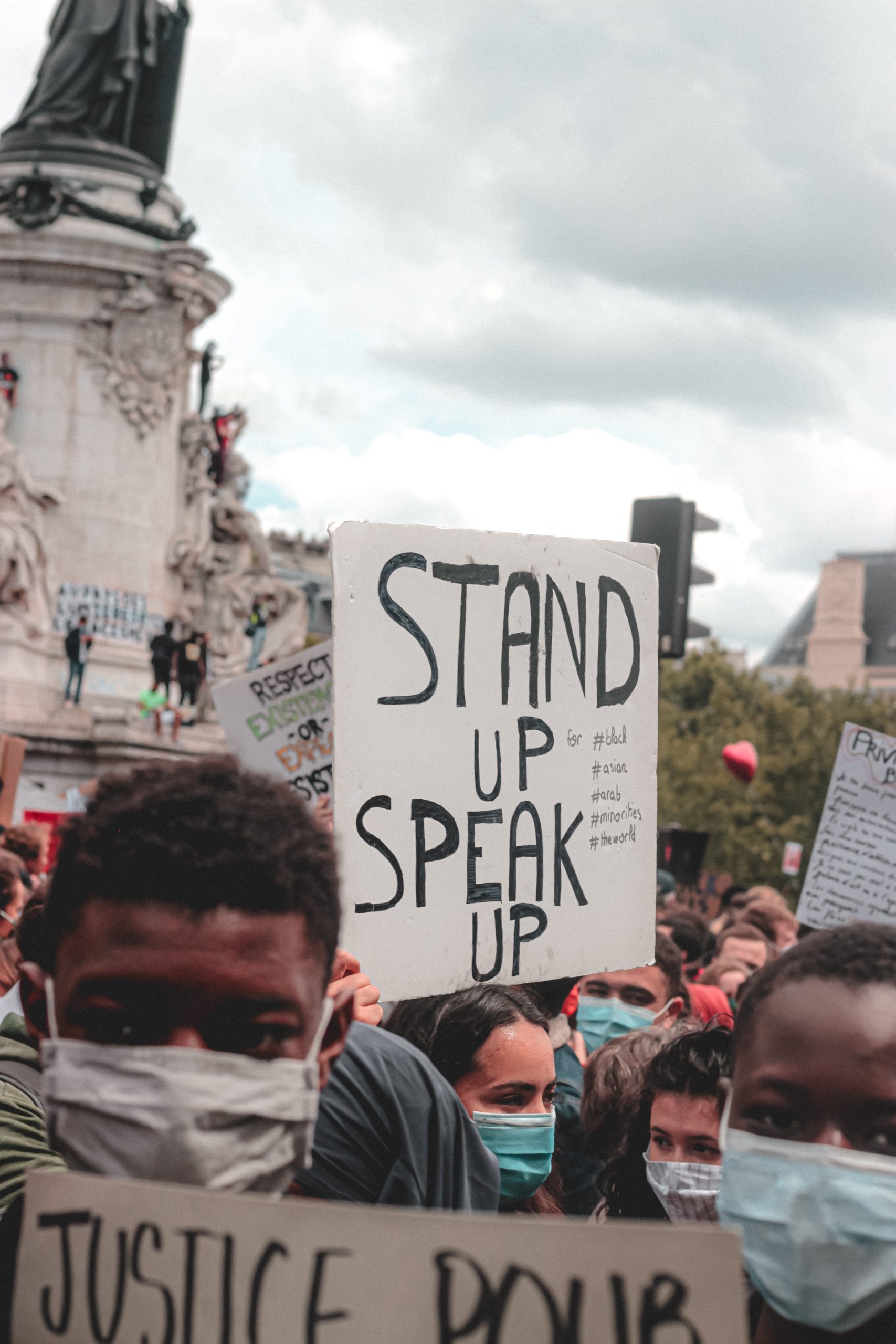 Someone holds up a poster reading "Stand Up, Speak Up"