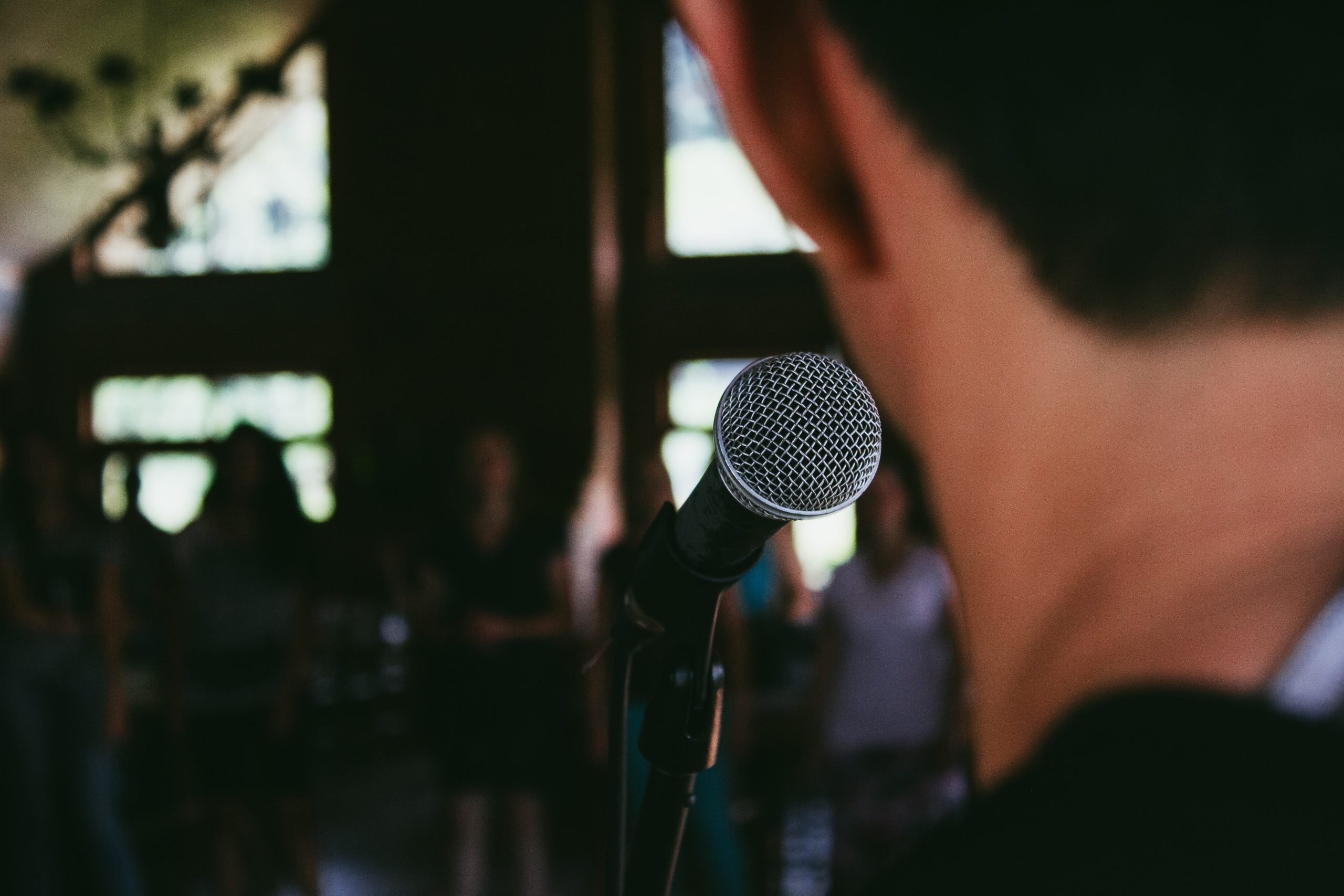 A young man stands in front of a microphone while looking into an audience