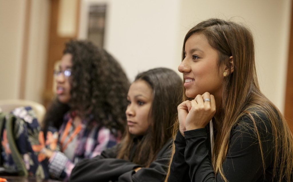 A young smiling female leans forward to indicate that she is listening.